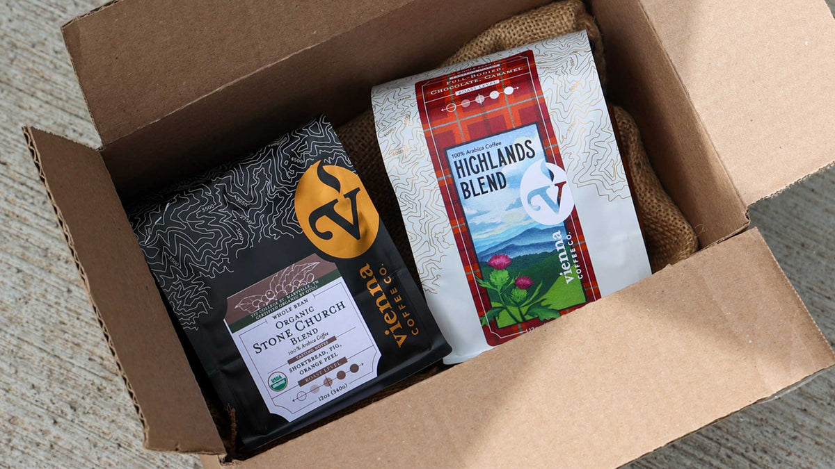 Open cardboard box for subscriptions containing two coffee packages, one labeled 'Highlands Blend' and the other with Organic Stone Church Blend